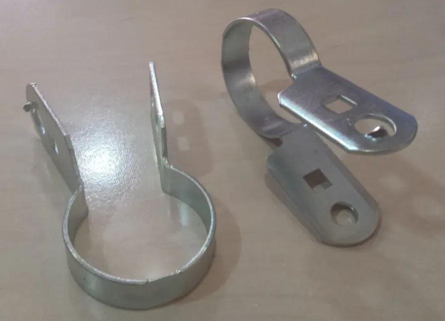 Dos clips para postes de cerca de metal galvanizado, cada uno con una banda circular y un extremo plano con agujeros.