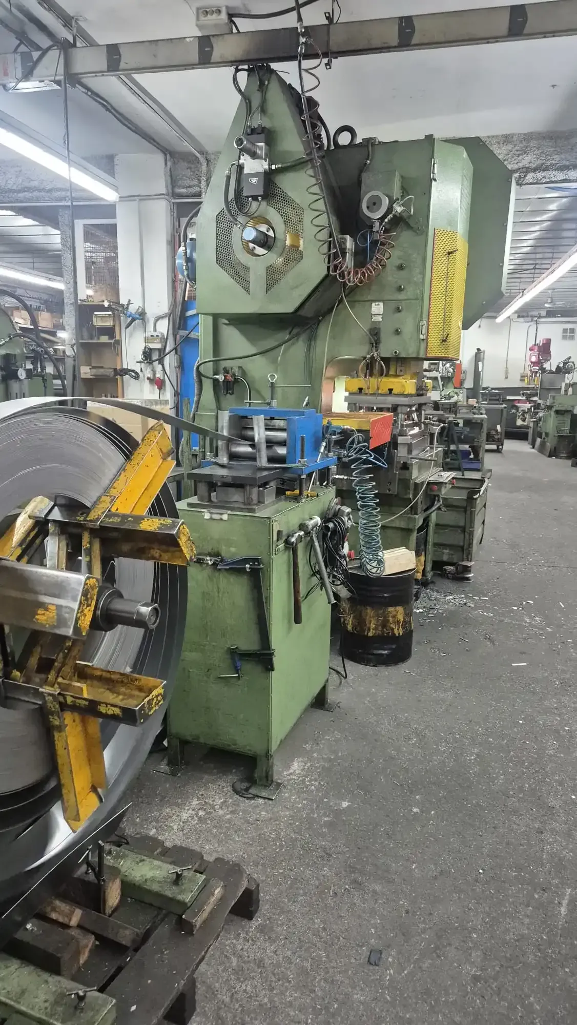 Gran prensa industrial en un taller de fábrica con piezas metálicas y maquinaria a su alrededor.