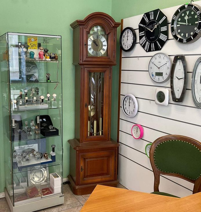 Verschiedene Uhren in einem Geschäft, mit einer hölzernen Standuhr und einer durchsichtigen Vitrine mit weiteren Uhren.