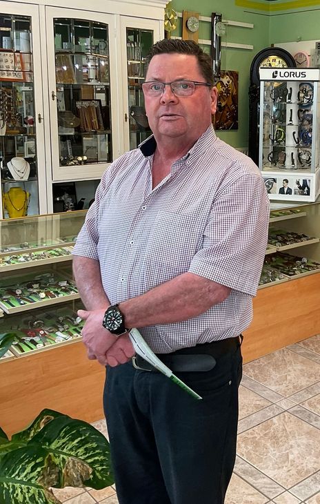 Inhaber Holger Häfke steht in seinem Geschäft, das im Hintergrund Schmuck und Uhren ausstellt.