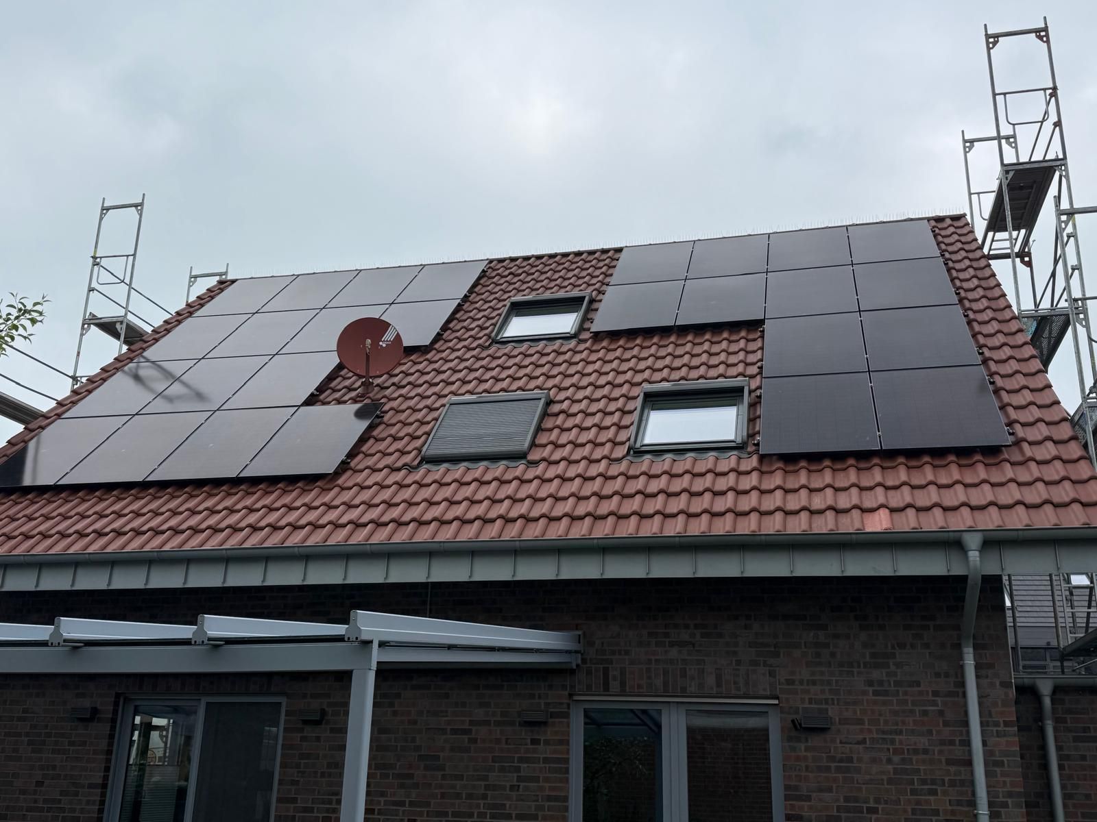 Auf dem roten Ziegeldach eines Backsteinhauses sind Solarpaneele installiert; Fenster, Satellitenschüssel und Gerüst sind ebenfalls vorhanden.