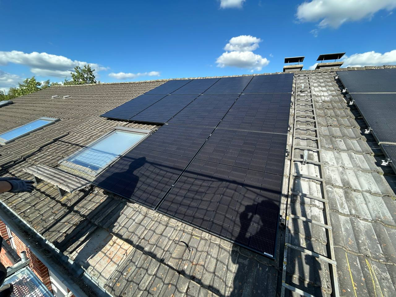 Auf einem verwitterten Ziegeldach unter einem teilweise bewölkten Himmel wurden Solarpaneele installiert.