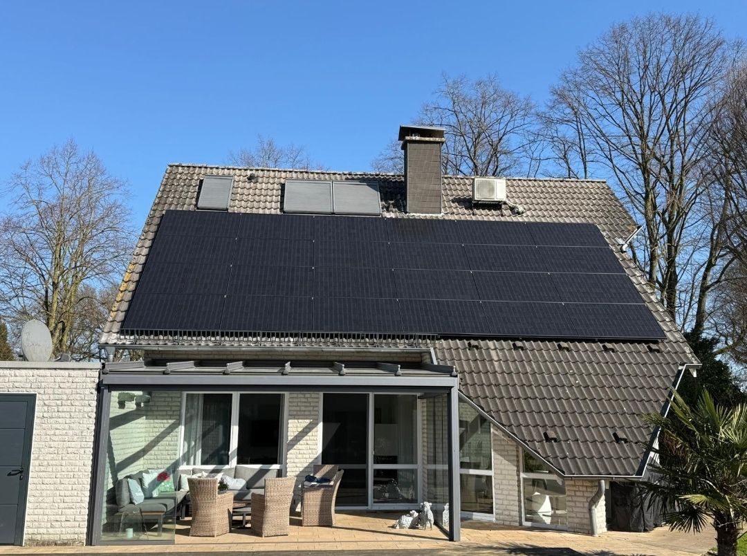 Haus mit Solarpaneelen auf dem Dach, einem verglasten Wintergarten und einem klaren blauen Himmel.