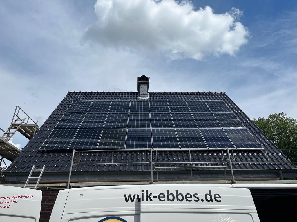 Solarpaneele, die auf einem schwarzen Dach eines Hauses unter einem bewölkten blauen Himmel installiert sind.