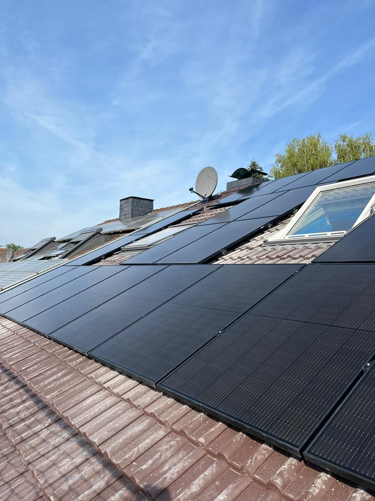 Solarpaneele auf einem mit Terrakotta-Ziegeln gedeckten Dach, mit Satellitenschüssel und Oberlicht, im Hintergrund blauer Himmel.