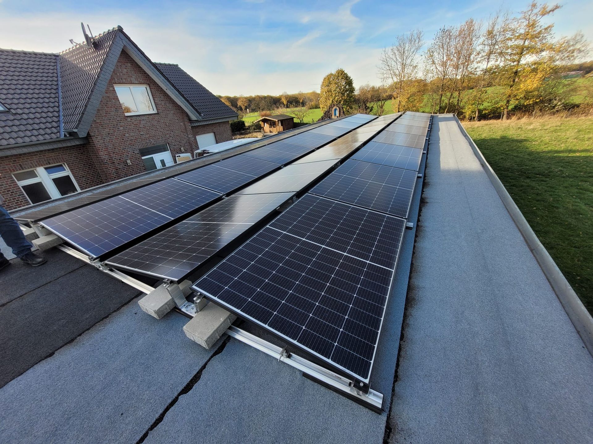 Solarpaneele, die an einem sonnigen Tag auf einem Flachdach neben einem Backsteinhaus installiert sind.