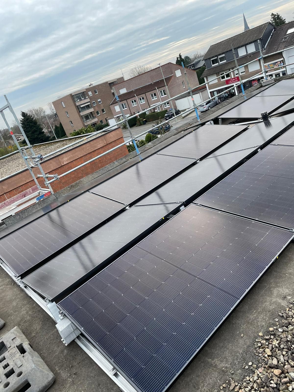 Auf einem Dach installierte Solarpaneele. Im Hintergrund Gebäude und bewölkter Himmel.