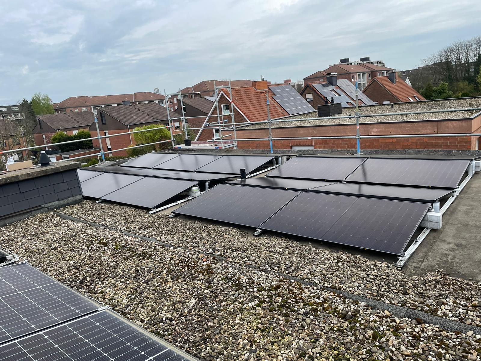 Solarpaneele auf dem Dach eines Gebäudes, im Hintergrund weitere Dächer und bewölkter Himmel.