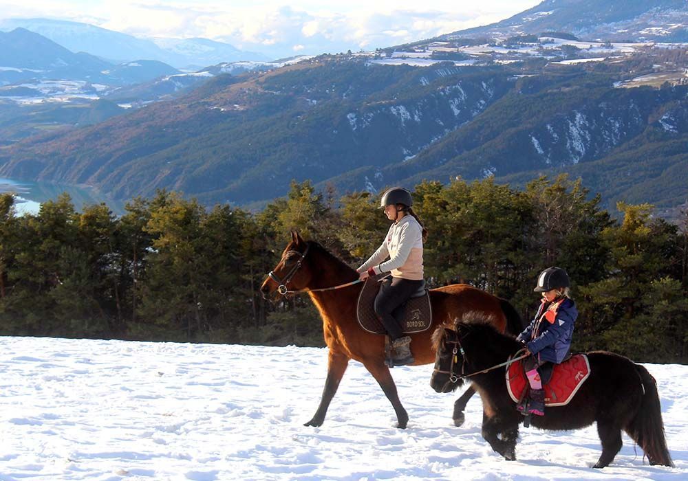 Deux cavaliers sur un sentier enneigé avec des montagnes en arrière-plan