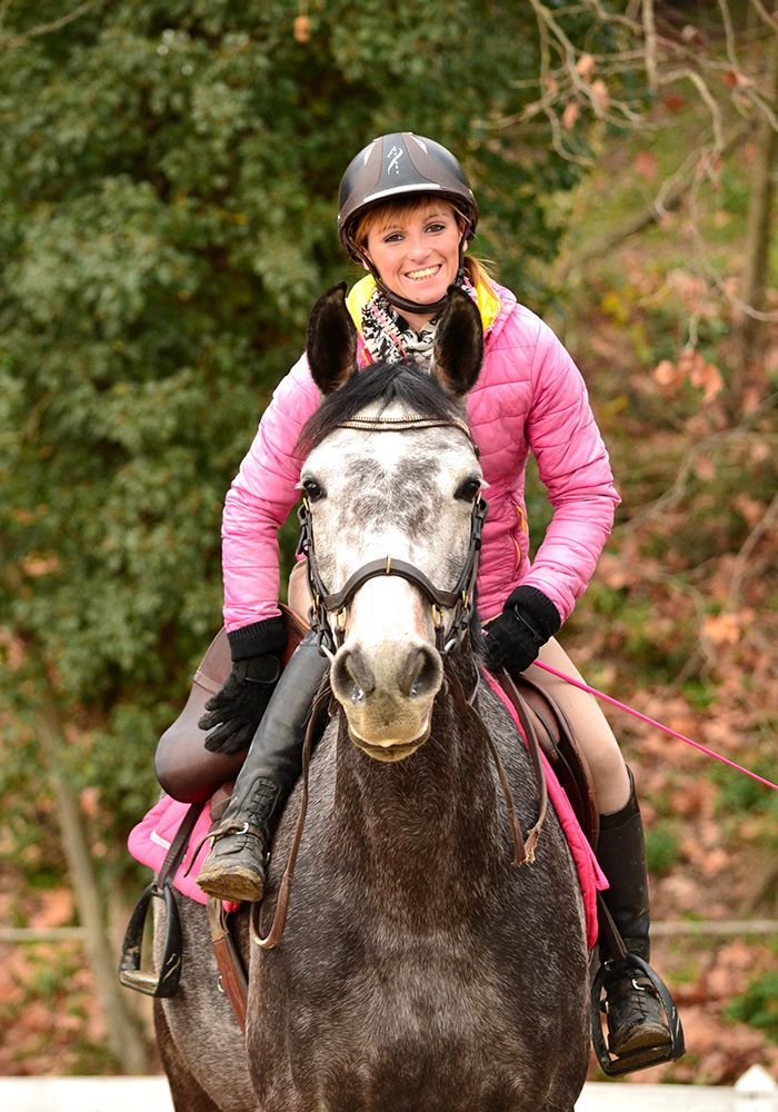 Cavalier souriant en veste rose sur un cheval noir, en extérieur sur un sentier boisé