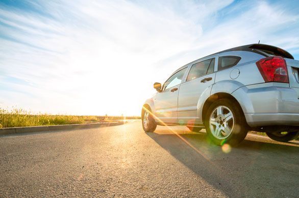 Un coche plateado está aparcado al costado de la carretera al atardecer.