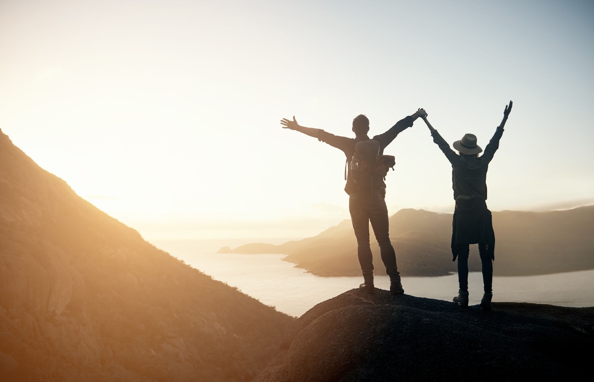 Dos personas están paradas en la cima de una montaña tomadas de la mano.