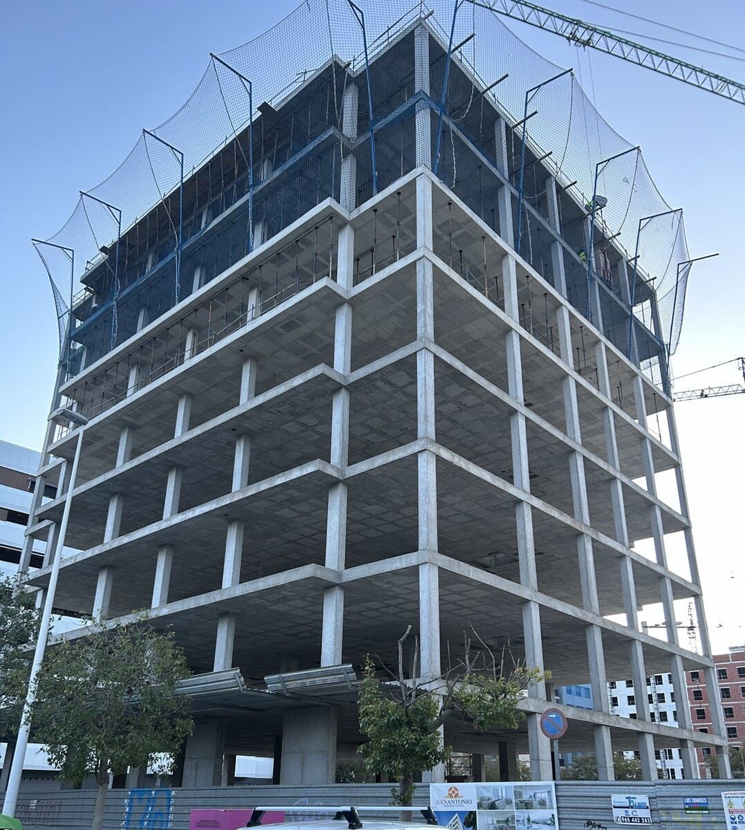Construcción de un edificio de varios pisos con estructura de hormigón, protegido por una red de seguridad de color azul.