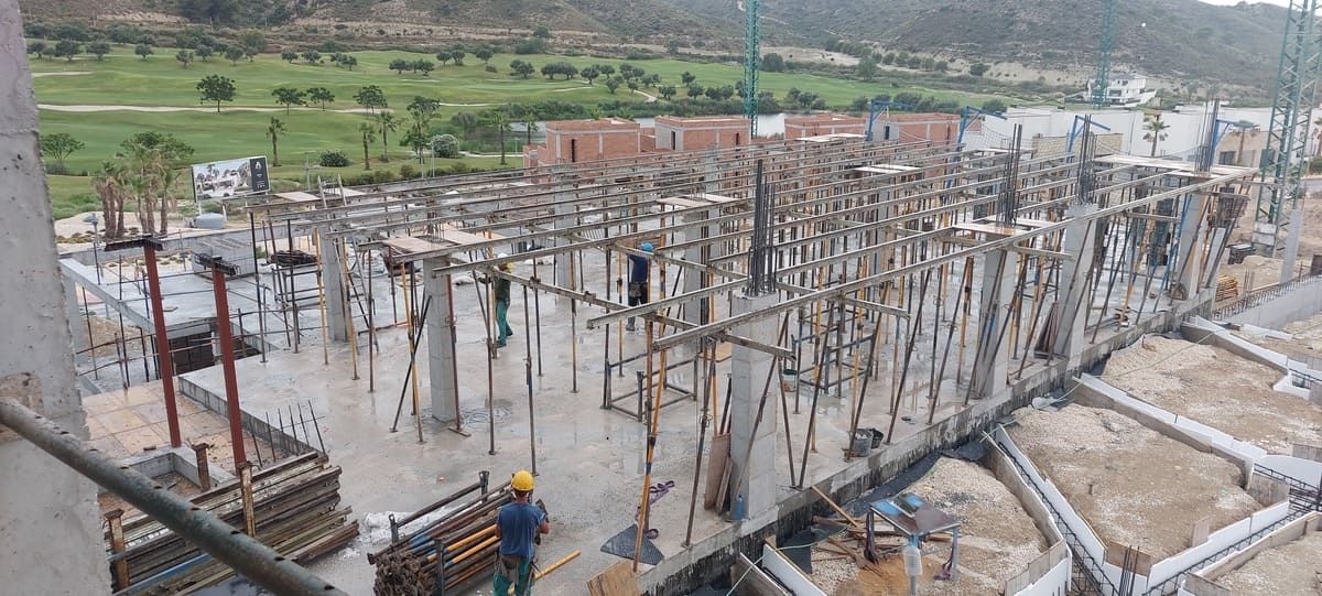 Sitio de construcción con pilares y andamios de hormigón, un trabajador y un fondo de paisaje verde.