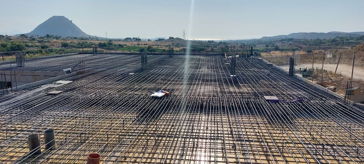 Sitio de construcción con una cuadrícula de barras de refuerzo de acero, montaña al fondo.