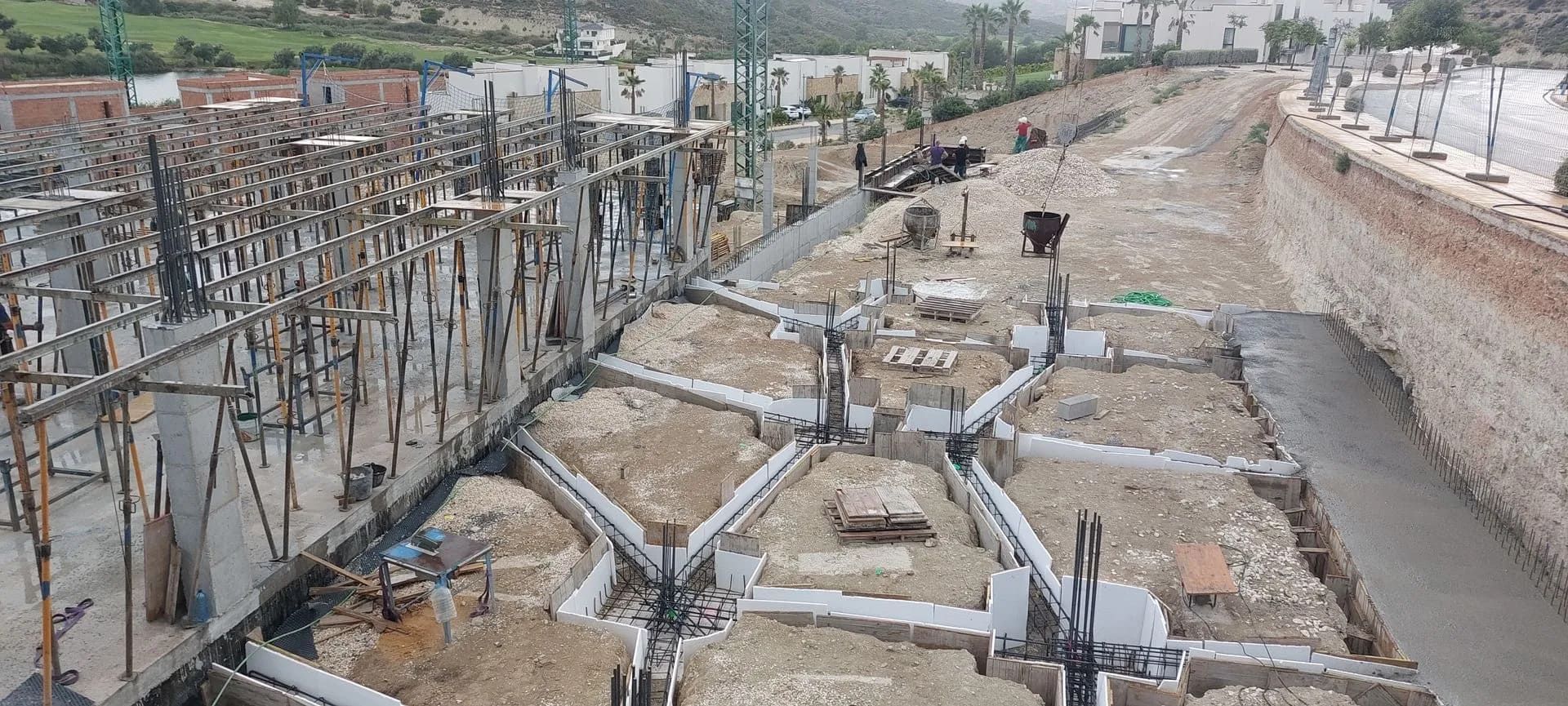 Sitio de construcción, encofrados de cimentación de hormigón, varillas de acero, trabajadores.