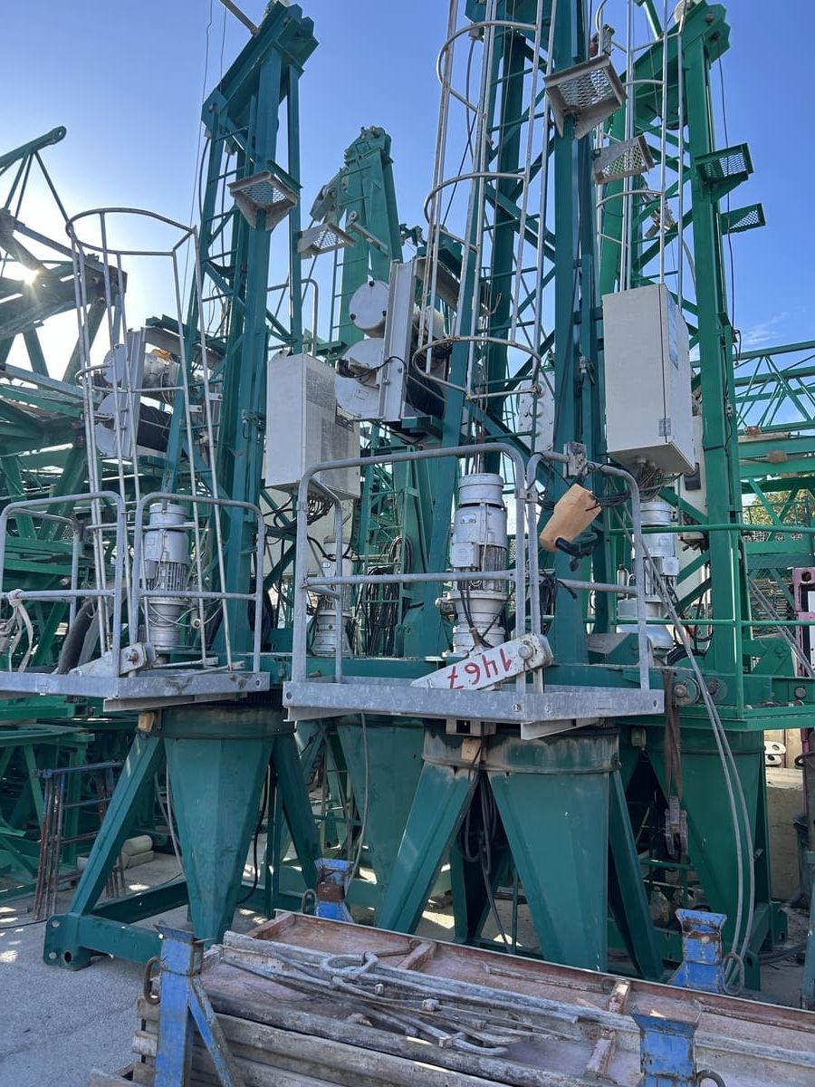 Maquinaria industrial verde con plataformas, cajas blancas y marcos de metal contra un cielo soleado.
