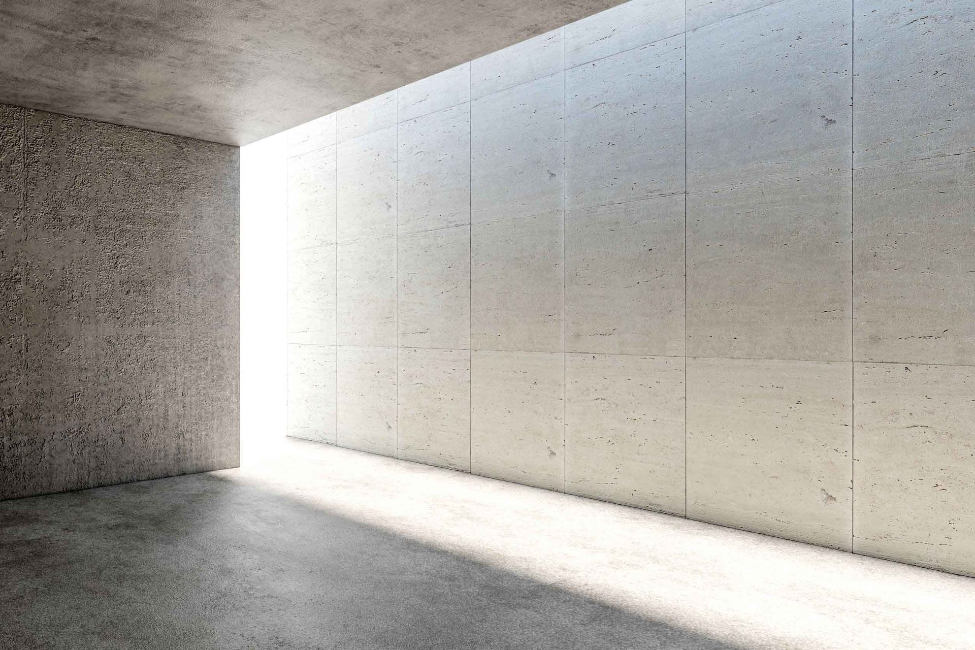 Habitación de hormigón con luz brillante que entra por una gran abertura. La luz del sol proyecta sombras en el suelo y las paredes.