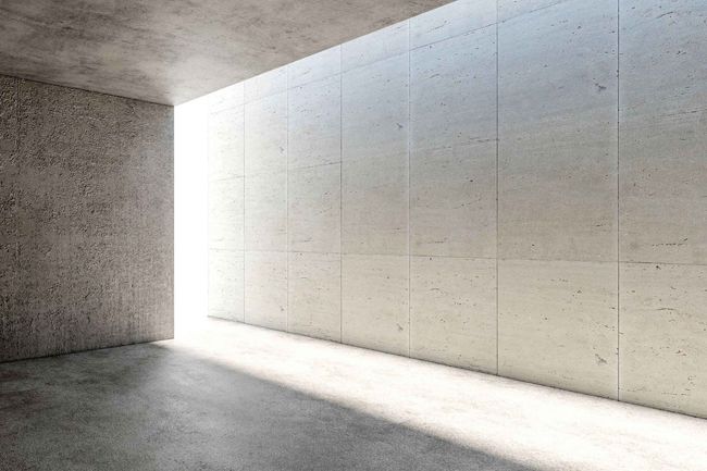 Habitación de hormigón con luz brillante que entra por una gran abertura. La luz del sol proyecta sombras en el suelo y las paredes.