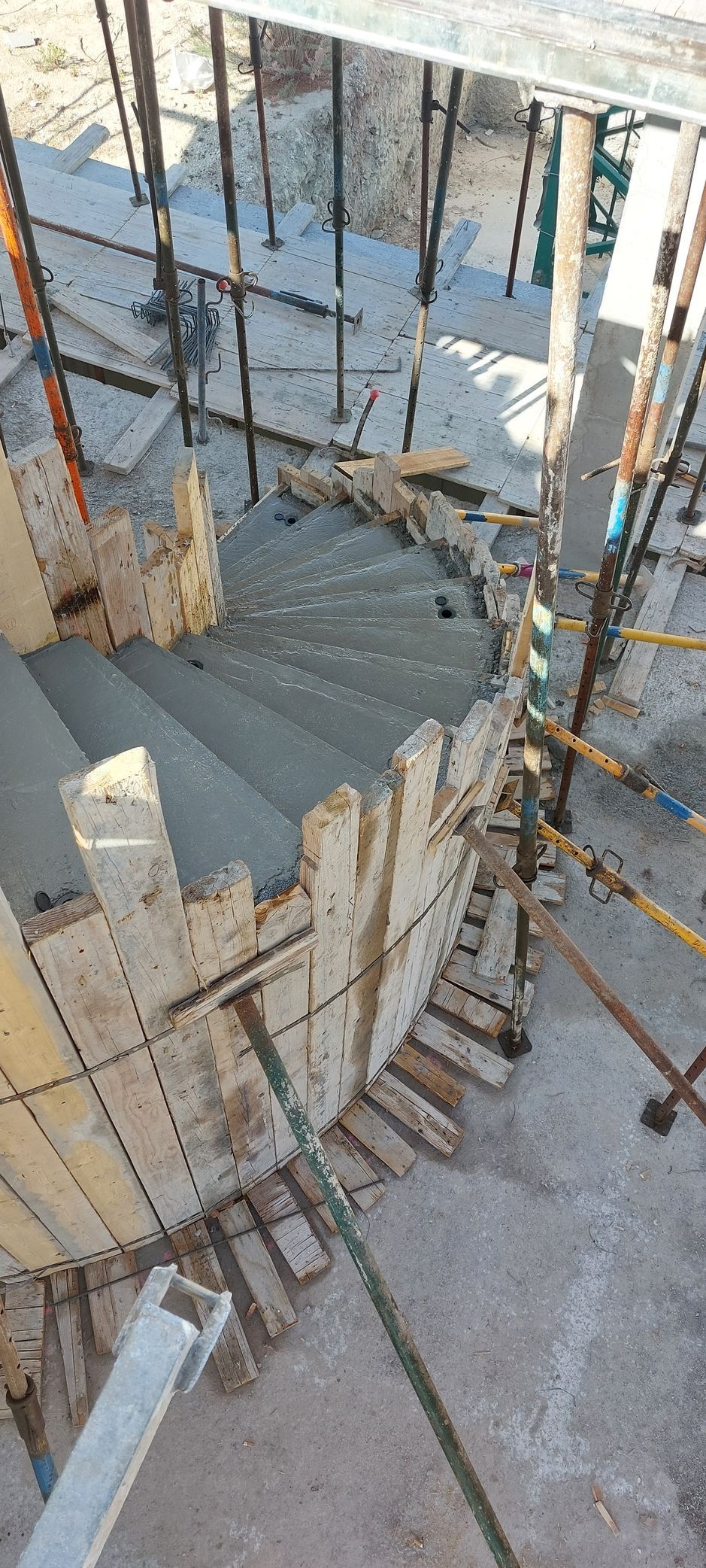 Obra con escalera circular en construcción, con peldaños de hormigón y encofrado de madera.