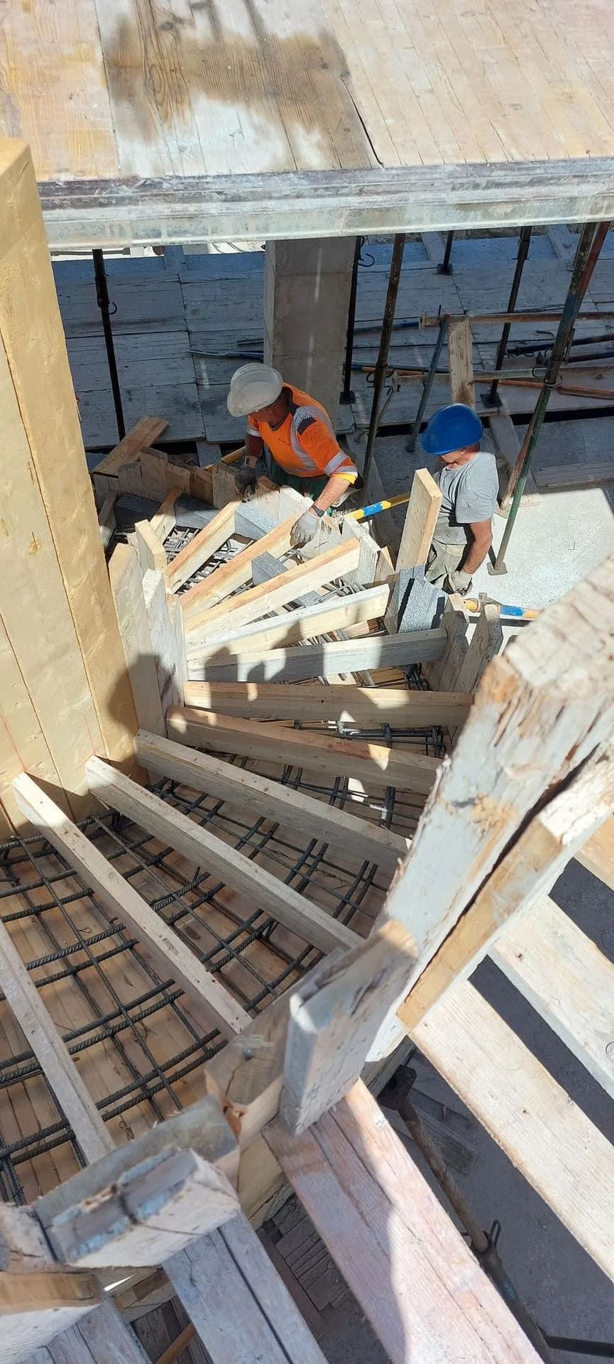 Obreros de la construcción construyen escaleras, utilizando madera y varillas de refuerzo.
