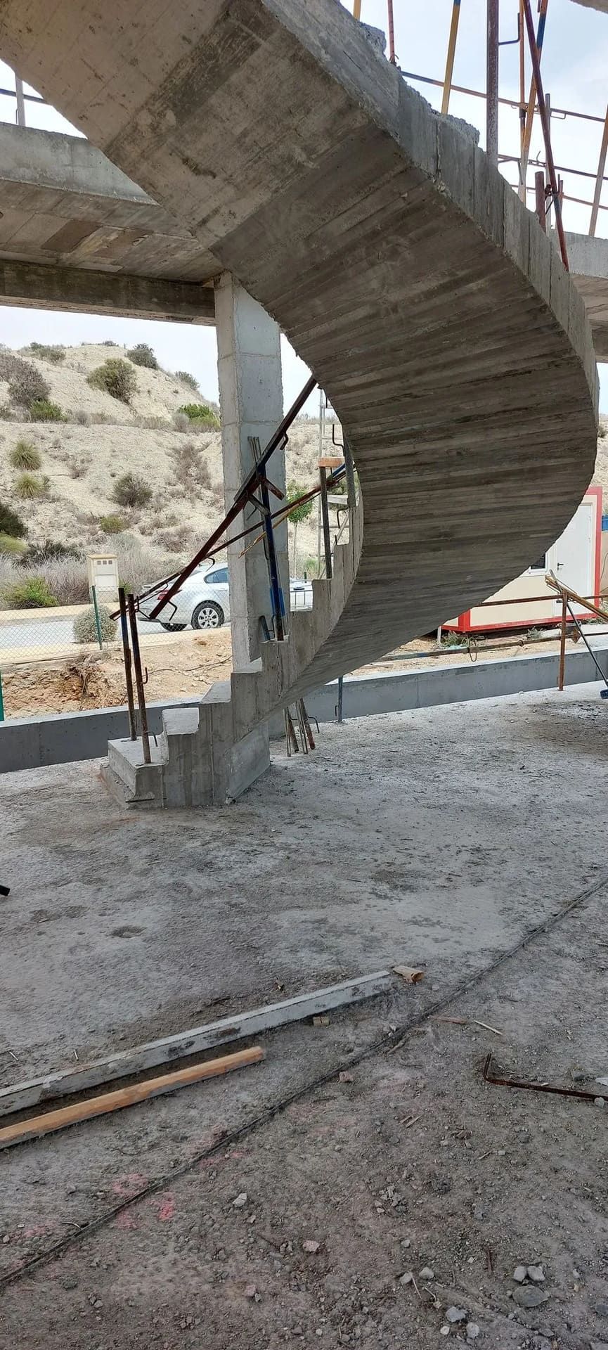 Escalera de caracol de hormigón en construcción, tonos grises, entorno exterior.