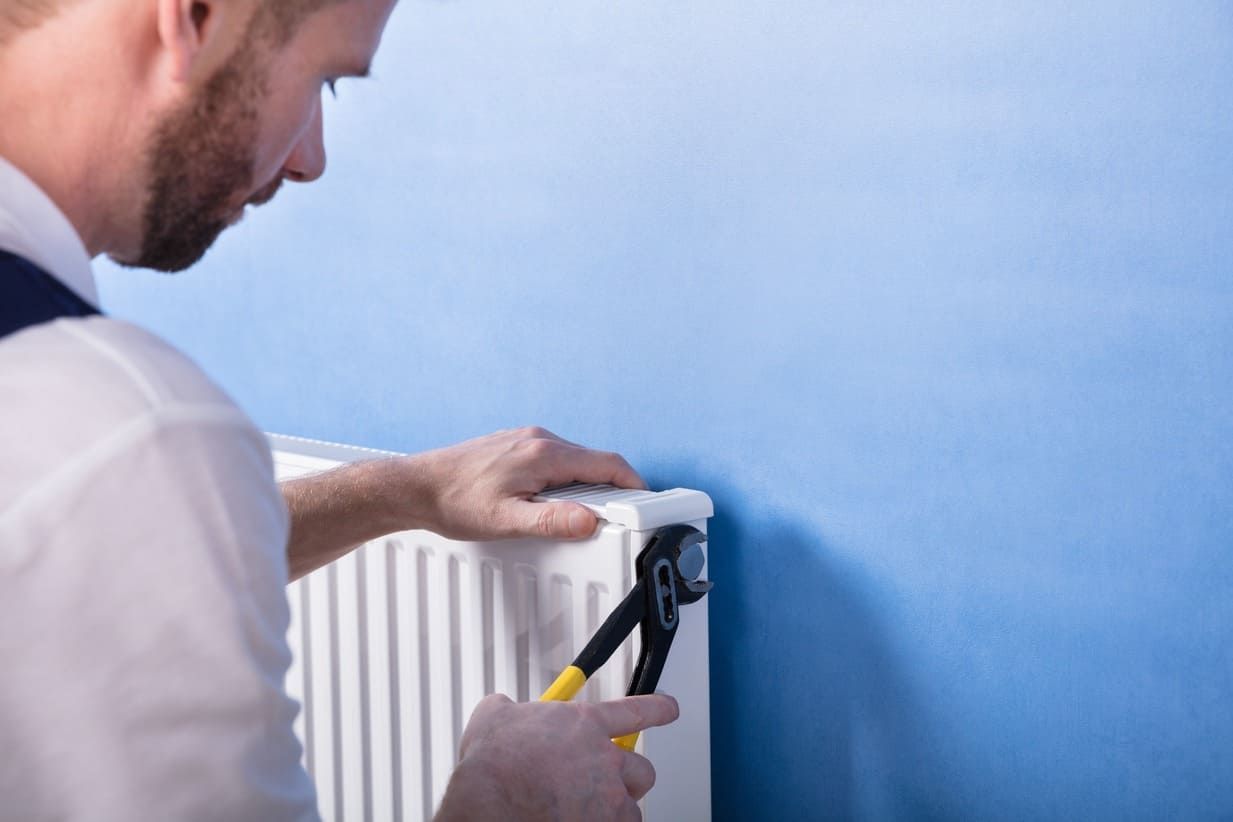 Un hombre está arreglando un radiador con un par de alicates.