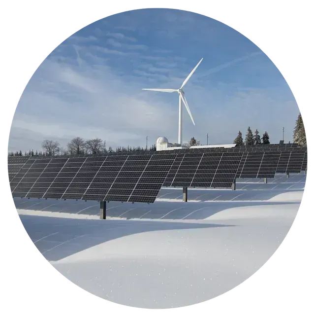 Una turbina eólica está situada junto a una fila de paneles solares en la nieve.