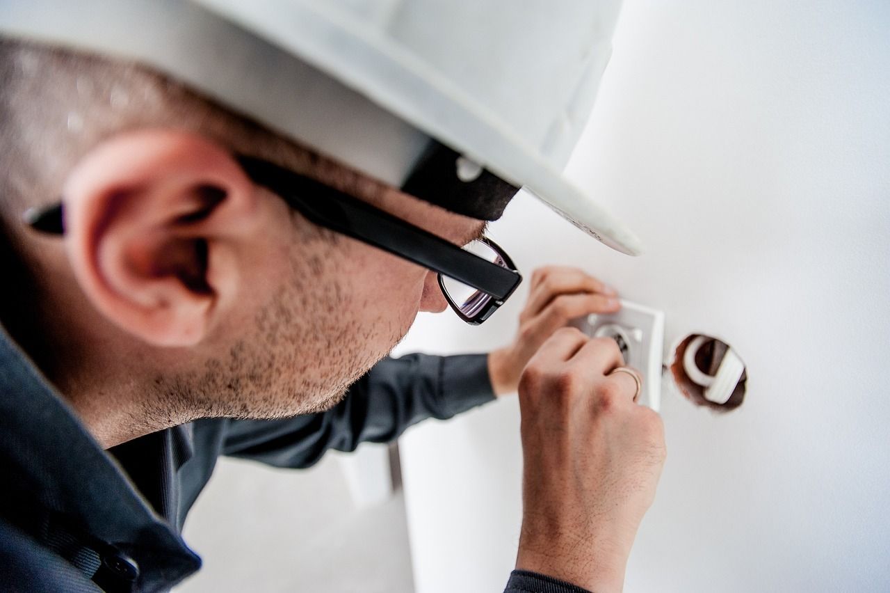 Un hombre que lleva casco y gafas está trabajando en una toma de corriente eléctrica.