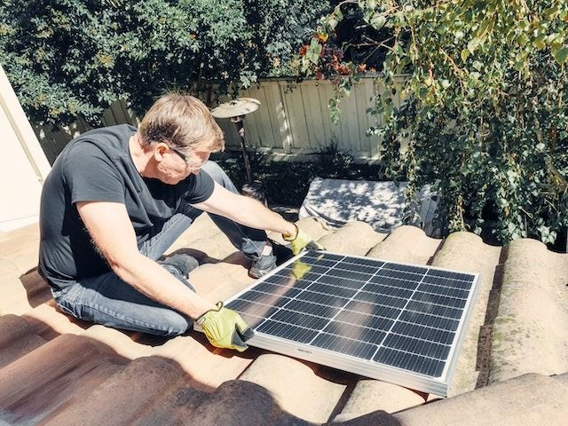Un hombre está instalando un panel solar en un techo de tejas.