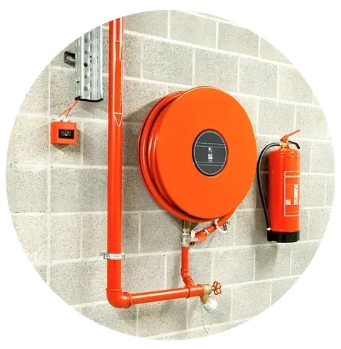 Una manguera contra incendios naranja está unida a una pared de ladrillos junto a un extintor rojo.