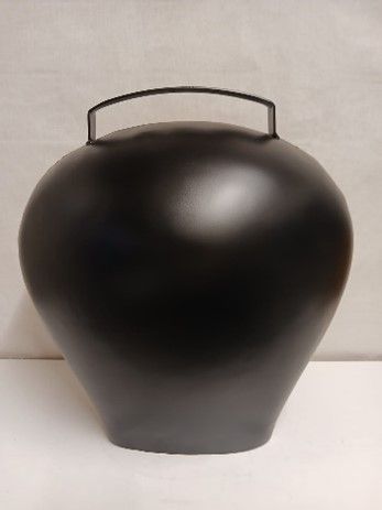 Auf einem Tisch steht eine schwarze Vase mit einem Gemälde darauf.