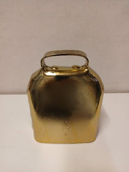 Auf einem weissen Tisch liegt eine kleine Messingglocke mit Griff.
