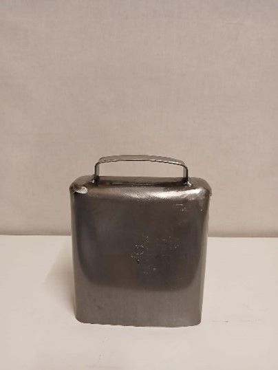 Auf einem weissen Tisch liegt eine kleine Messingglocke mit Griff.