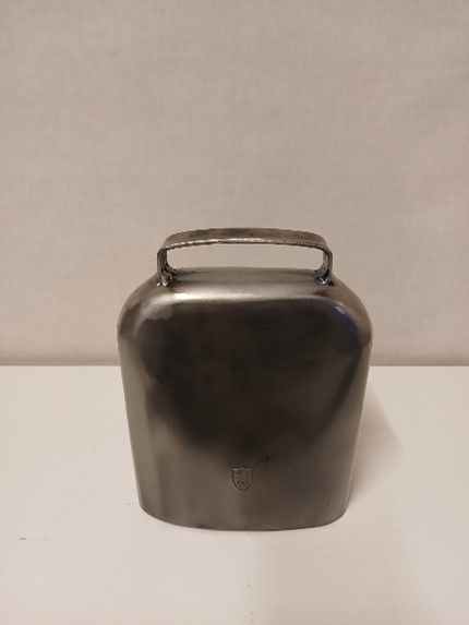 Auf einem weißen Tisch liegt eine Metallglocke mit Griff.