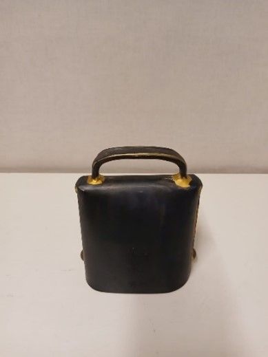 Auf einem weißen Tisch liegt eine schwarze Handtasche mit goldenem Griff.