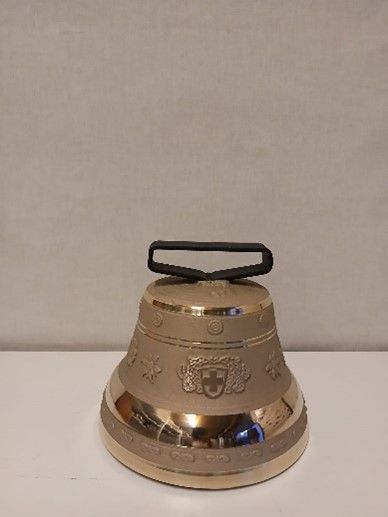 Auf einem weißen Tisch liegt eine Messingglocke mit schwarzem Griff.