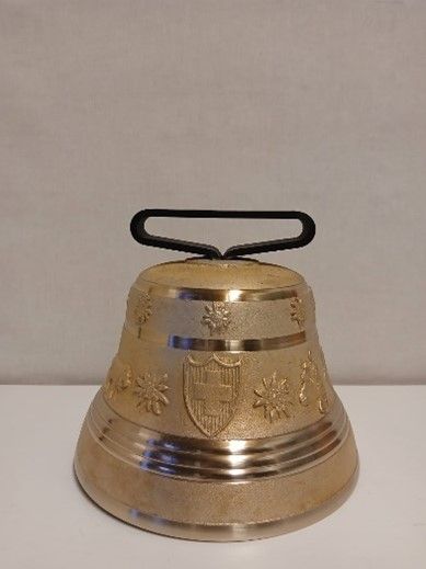 Auf einem weißen Tisch liegt eine Messingglocke mit schwarzem Griff.