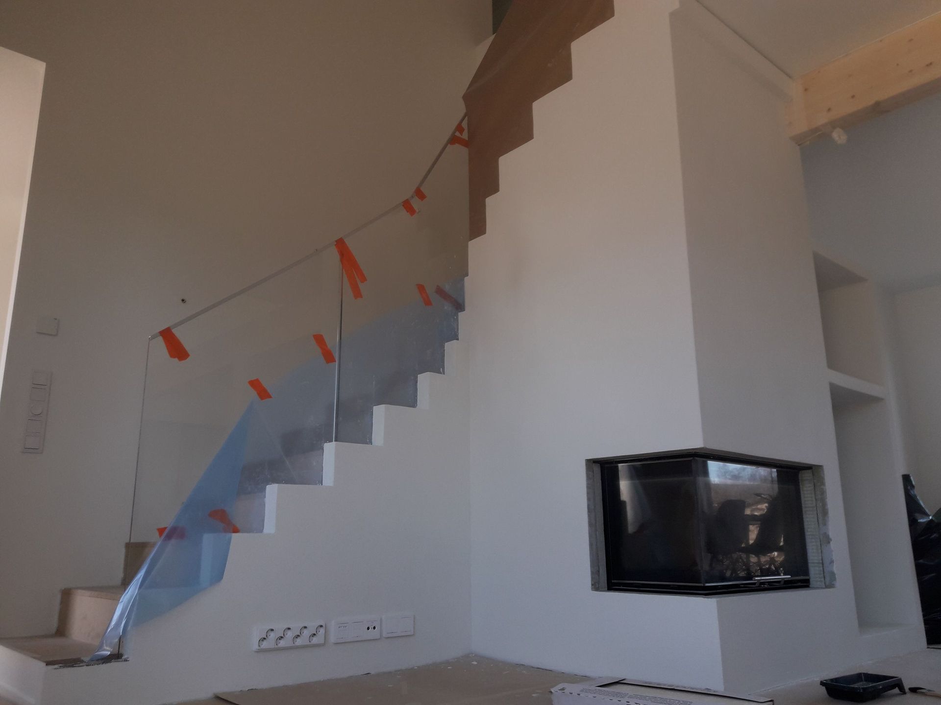 Moderni sisäportaikko, jossa lasikaide ja valkoiseen seinään rakennettu takka.