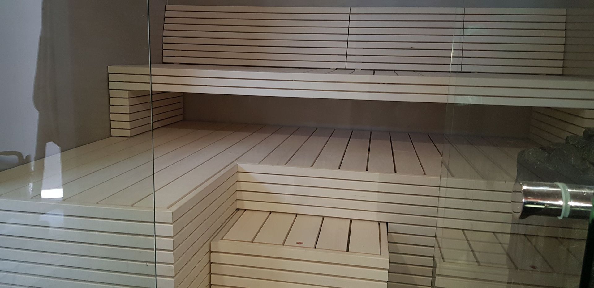 Sisäkuva puisesta saunahuoneesta, jossa on porrastetut penkit ja vaaleat sälepohjaiset puuseinät.