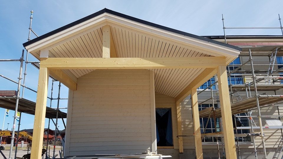 Uudelleen rakennettu, vaalea puinen kuisti, joka on kiinnitetty rakennustelineillä rakenteilla olevaan taloon.