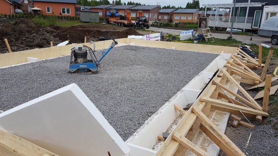 Rakennustyömaa, jossa näkyy valkoisista vaahtomuovilahoista tehty perustusymmetria, täytetty soralla ja puisilla tukipalkeilla.