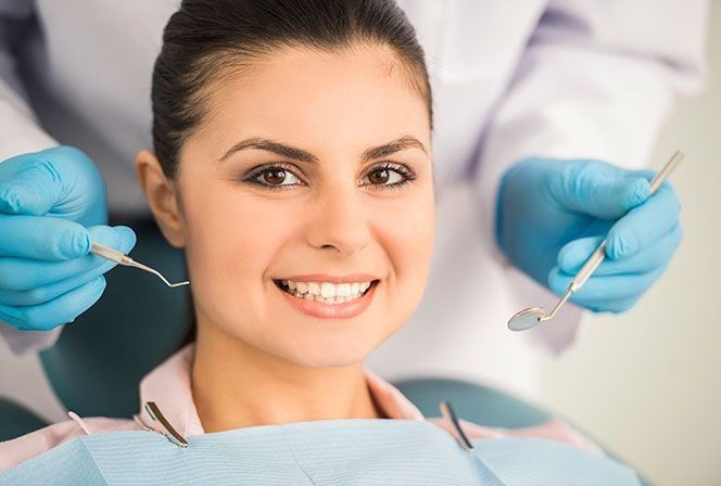 Una mujer está sentada en una silla dental mientras un dentista le examina los dientes.