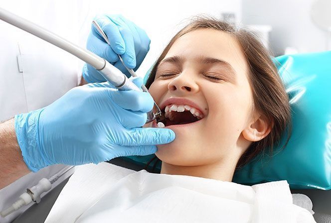 A una niña le están examinando los dientes un dentista.