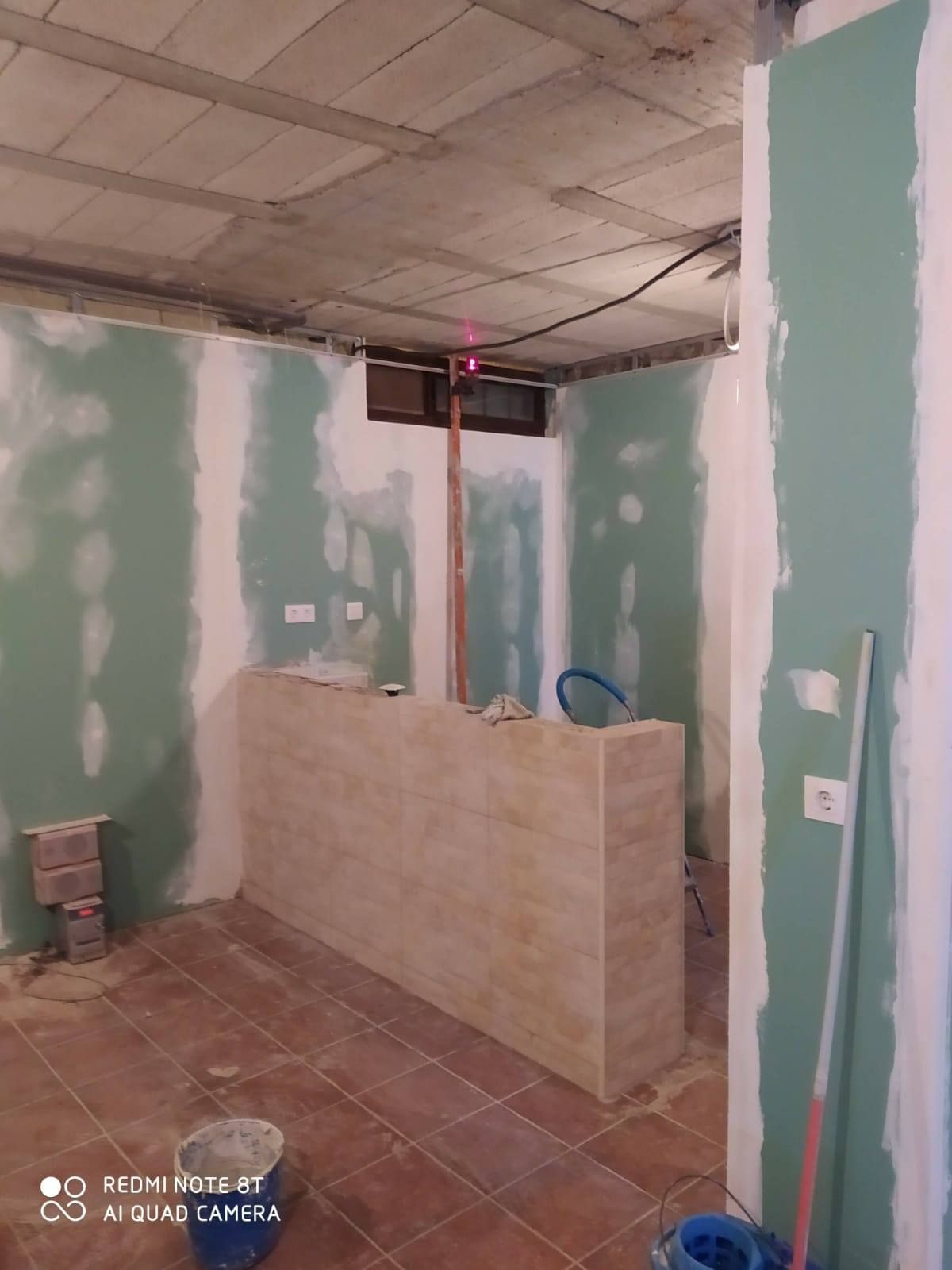 Construcción interior: habitación con piso de baldosas, paneles de yeso, barra sin terminar y techo expuesto.