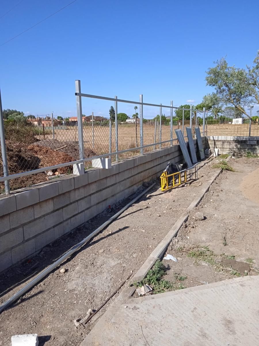 Sitio de construcción con muro de bloques de hormigón, valla metálica y materiales de construcción.