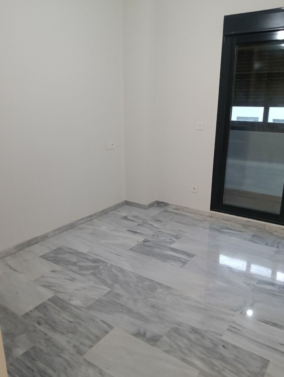 Habitación vacía con suelo de mármol gris y una ventana de marco oscuro.