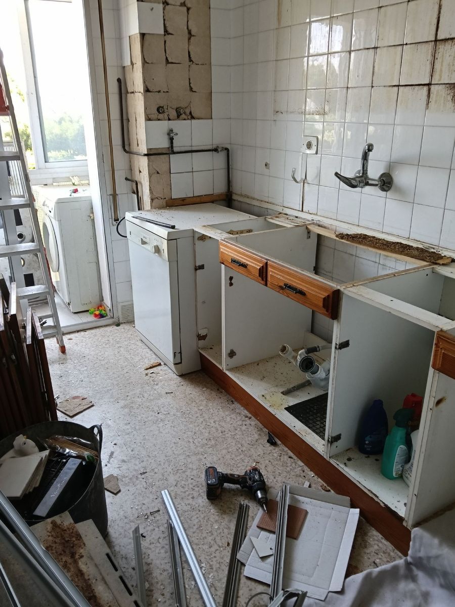 Renovación de cocina en progreso, con gabinetes parcialmente removidos, paredes expuestas y escombros.