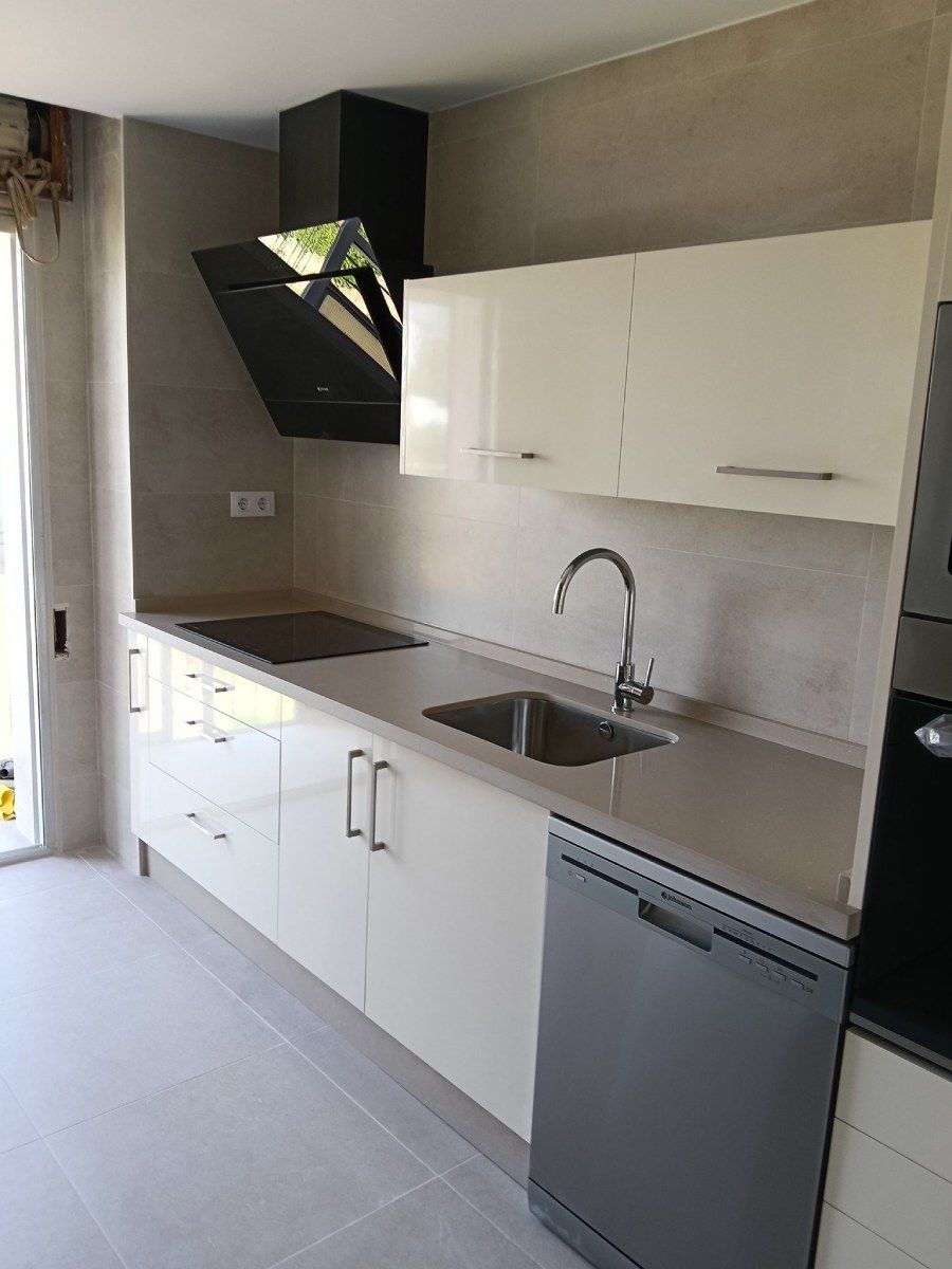 Cocina moderna con gabinetes blancos, electrodomésticos de acero inoxidable y encimera gris.