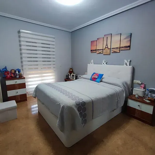 Un dormitorio con una cama, mesitas de noche y cuadros en la pared.